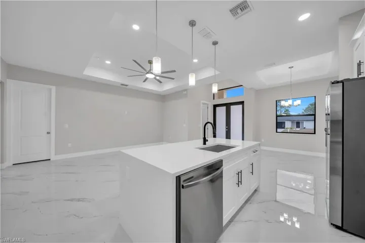 Kitchen featuring white cabinets, a raised ceiling, appliances with stainless steel finishes, decorative light fixtures, and recessed lighting