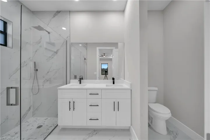 Full bathroom with a marble finish shower, double vanity, light marble finish floors, and ceiling fan