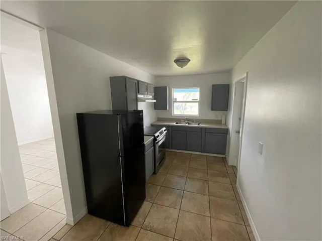 Kitchen with black fridge, gray cabinetry, light tile flooring, and stainless steel range with electric cooktop