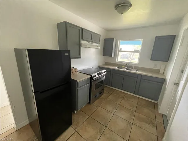 Kitchen featuring black fridge, sink, stainless steel electric range oven, and light tile flooring