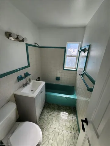 Full bathroom with tile walls, tile flooring, vanity, and toilet