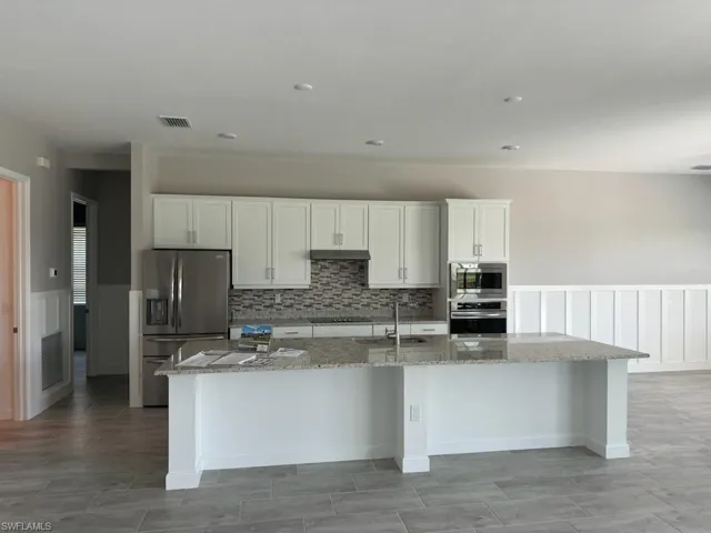 Kitchen with white cabinets, stainless steel appliances, light stone counters, and a center island with sink