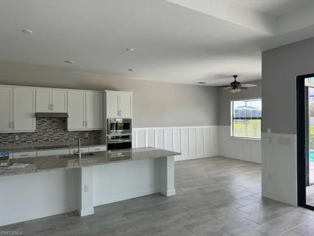 Kitchen with stainless steel appliances, sink, light stone countertops, white cabinetry, and ceiling fan
