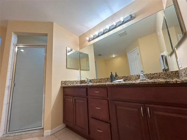 Bathroom featuring a stall shower, tile patterned floors, double vanity, and baseboards