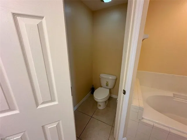 Bathroom featuring toilet, a garden tub, tile patterned floors, and baseboards