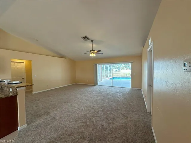 Unfurnished living room featuring ceiling fan, vaulted ceiling, light colored carpet, and baseboards
