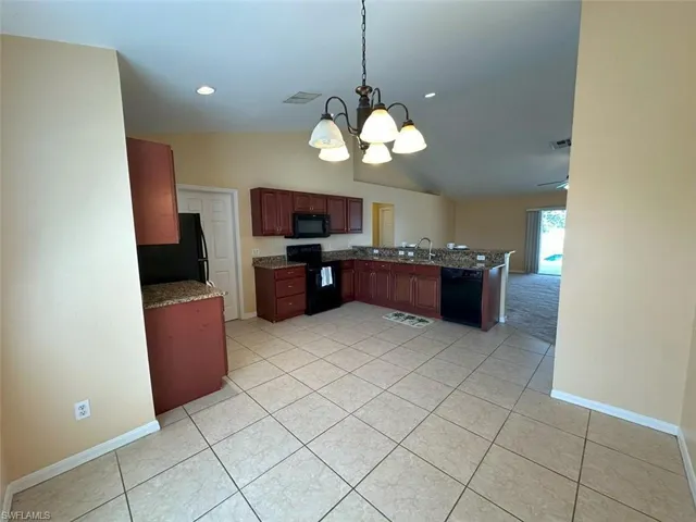 Kitchen with black appliances, a chandelier, vaulted ceiling, baseboards, and light tile patterned flooring