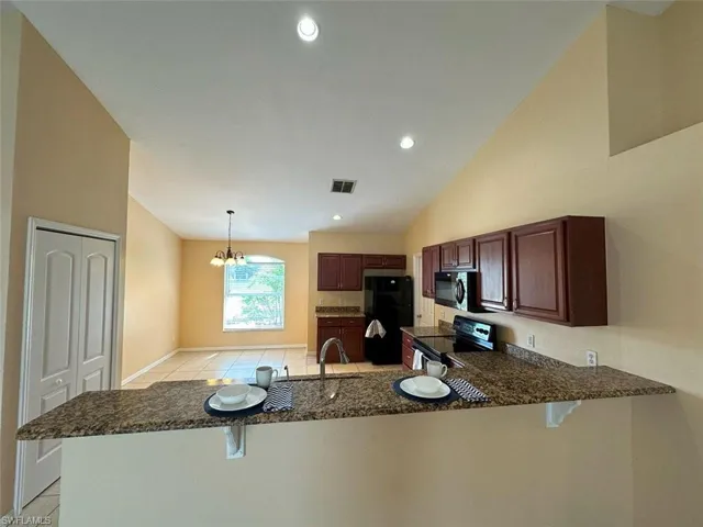 Kitchen with black appliances, a breakfast bar, a peninsula, a chandelier, and dark stone countertops