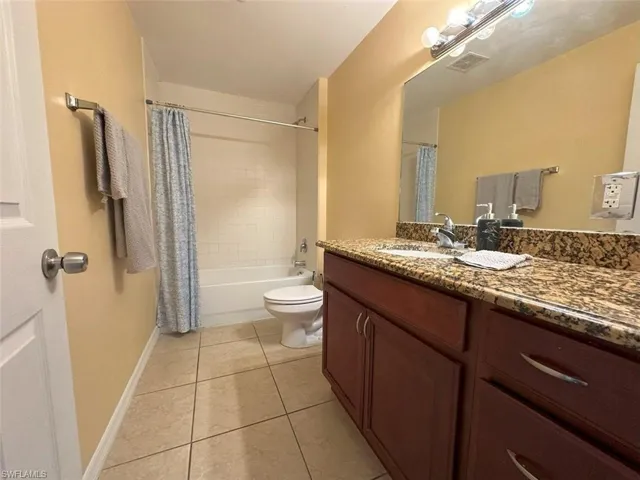 Full bathroom featuring tile patterned flooring, toilet, vanity, baseboards, and shower / bath combination with curtain
