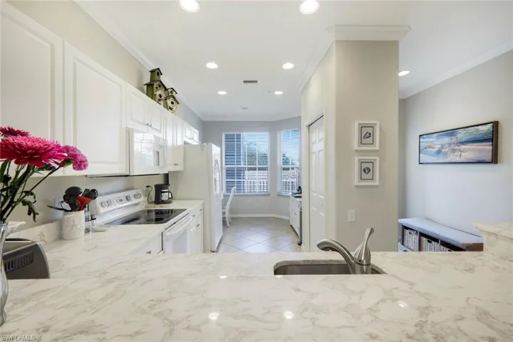 Kitchen featuring white appliances, white cabinets, crown molding, recessed lighting, and light tile patterned flooring
