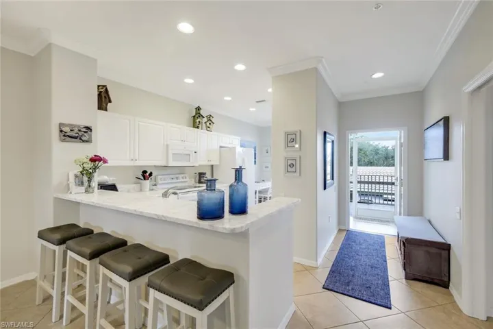 Kitchen with a breakfast bar area, a peninsula, white cabinetry, white appliances, and recessed lighting