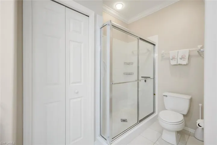 Full bath with a closet, ornamental molding, a shower stall, and light tile patterned floors