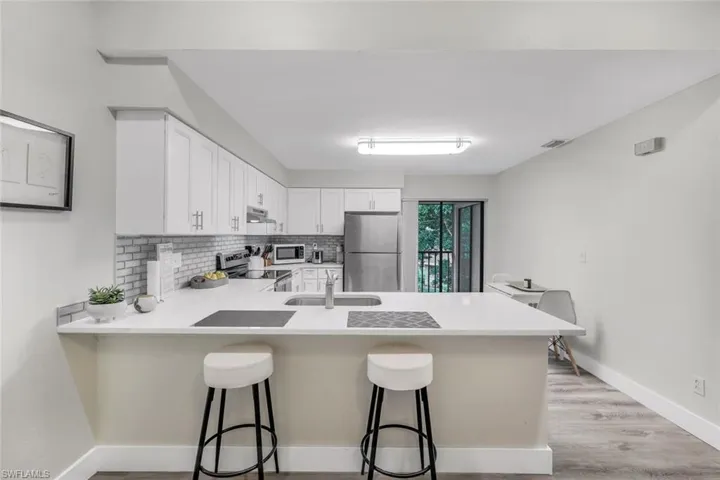 Kitchen with appliances with stainless steel finishes, a sink, a peninsula, decorative backsplash, and light countertops