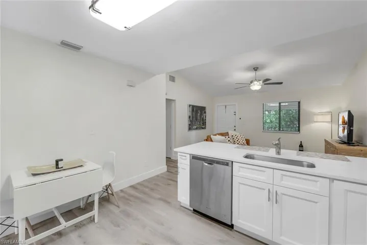 Kitchen featuring stainless steel dishwasher, a sink, lofted ceiling, light wood-style floors, and white cabinetry