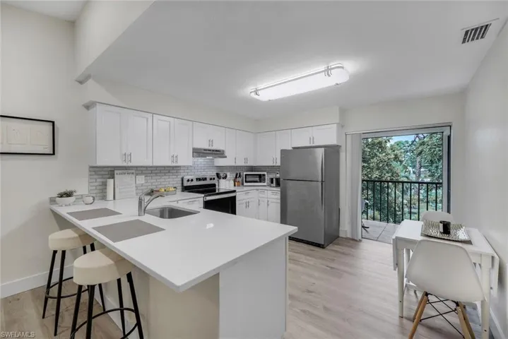 Kitchen with stainless steel appliances, a sink, under cabinet range hood, a peninsula, and light countertops