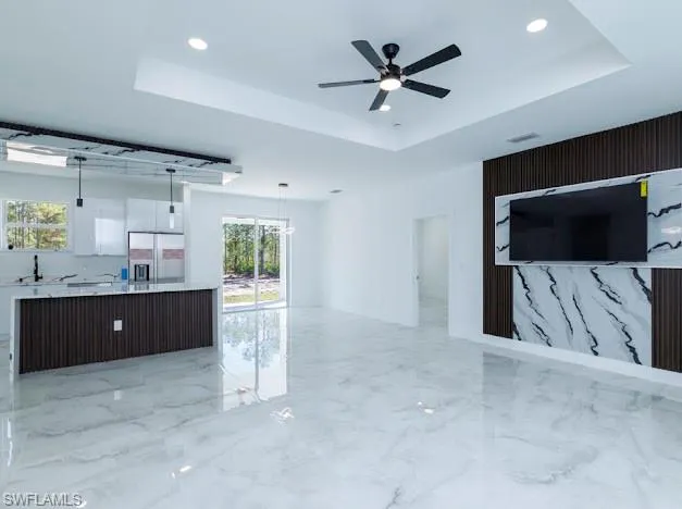 Unfurnished living room featuring a tray ceiling, light marble finish floors, recessed lighting, and a ceiling fan
