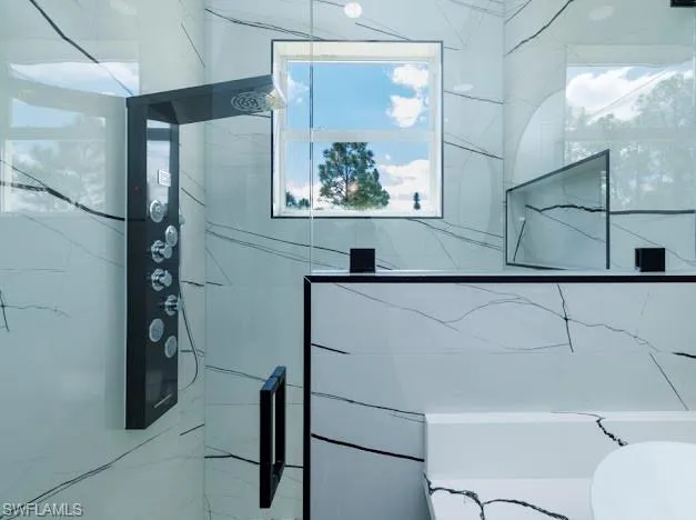 Full bathroom with a marble finish shower and toilet