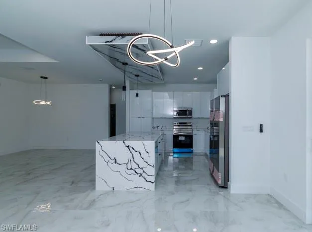 Kitchen with appliances with stainless steel finishes, white cabinets, a chandelier, hanging light fixtures, and light marble finish floors