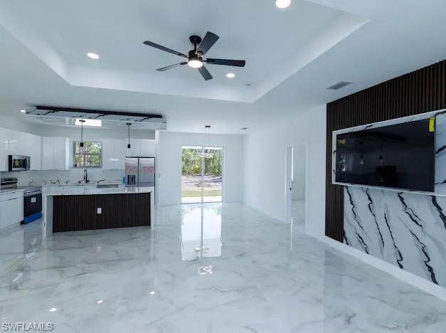 Kitchen featuring stainless steel appliances, white cabinets, modern cabinets, a tray ceiling, and a center island
