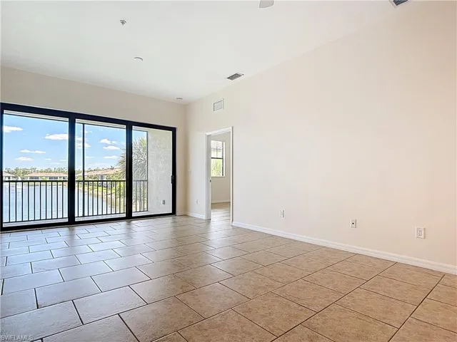 Empty room with light tile patterned flooring, visible vents, baseboards, and a water view