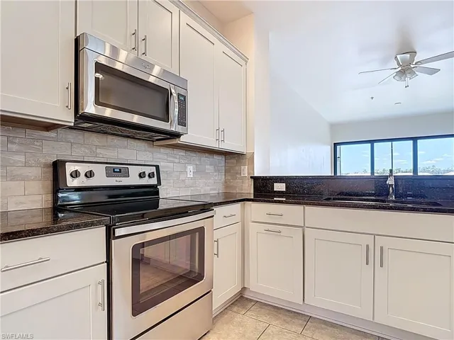 Kitchen featuring a sink, dark stone counters, decorative backsplash, a ceiling fan, and appliances with stainless steel finishes