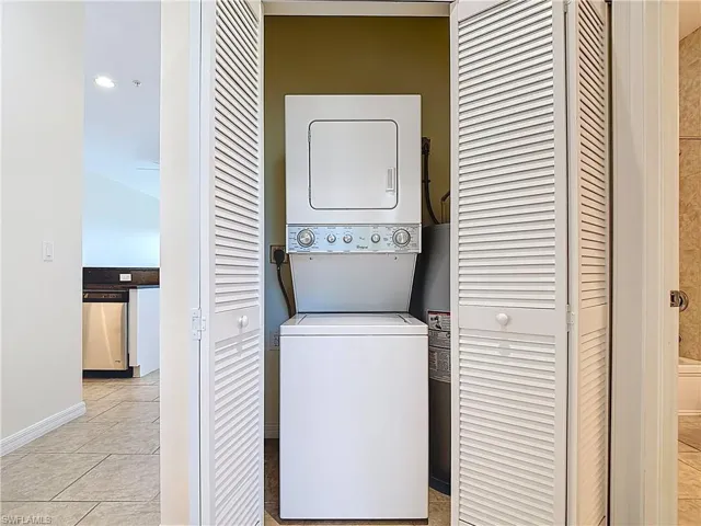 Laundry room with light tile patterned floors, stacked washing maching and dryer, baseboards, and laundry area