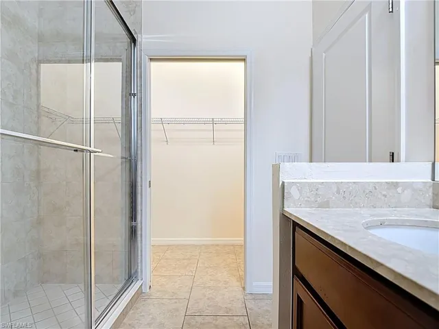 Full bathroom with a shower stall, tile patterned floors, vanity, a walk in closet, and baseboards