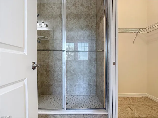 Full bathroom with a spacious closet, baseboards, tile patterned floors, and a stall shower