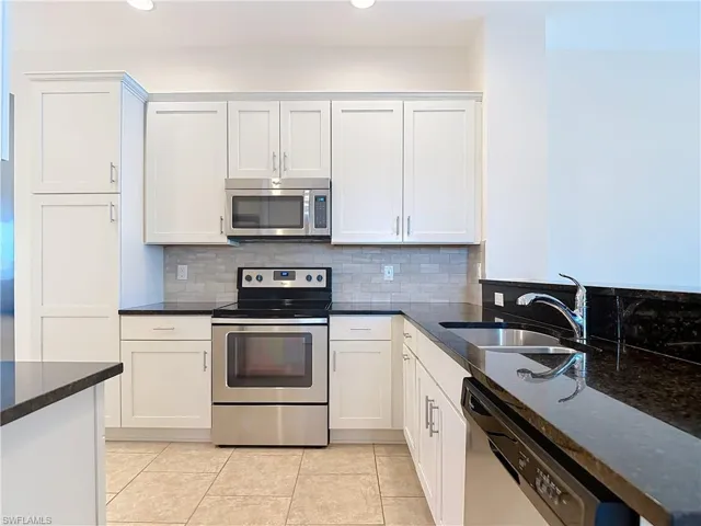 Kitchen with dark stone counters, tasteful backsplash, a sink, light tile patterned floors, and appliances with stainless steel finishes
