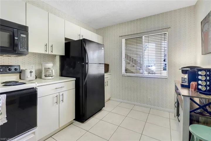 Kitchen featuring black appliances, white cabinets, light tile patterned floors, and a textured ceiling