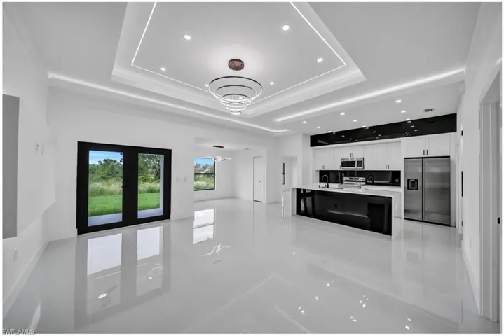 Unfurnished living room with a tray ceiling, recessed lighting, a chandelier, french doors, and light tile patterned flooring