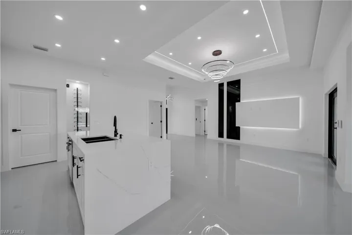 Kitchen with recessed lighting, a tray ceiling, open floor plan, an island with sink, and light stone counters