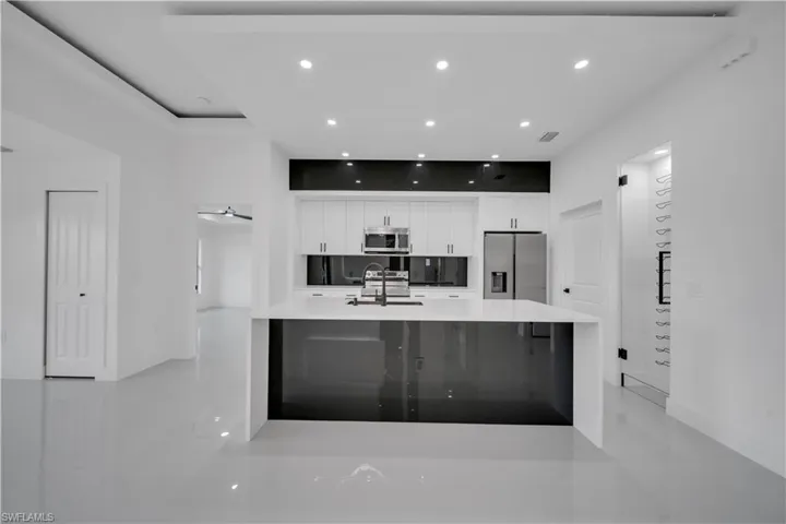 Kitchen featuring stainless steel appliances, white cabinetry, light countertops, a large island with sink, and recessed lighting