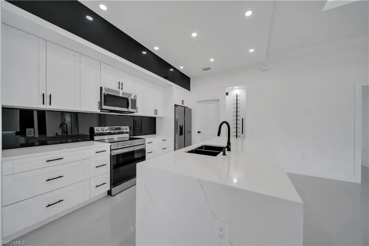 Kitchen with stainless steel appliances, a center island with sink, recessed lighting, white cabinetry, and light countertops