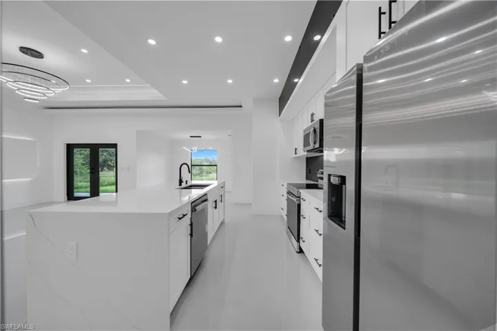 Kitchen with appliances with stainless steel finishes, white cabinetry, a large island, a raised ceiling, and recessed lighting