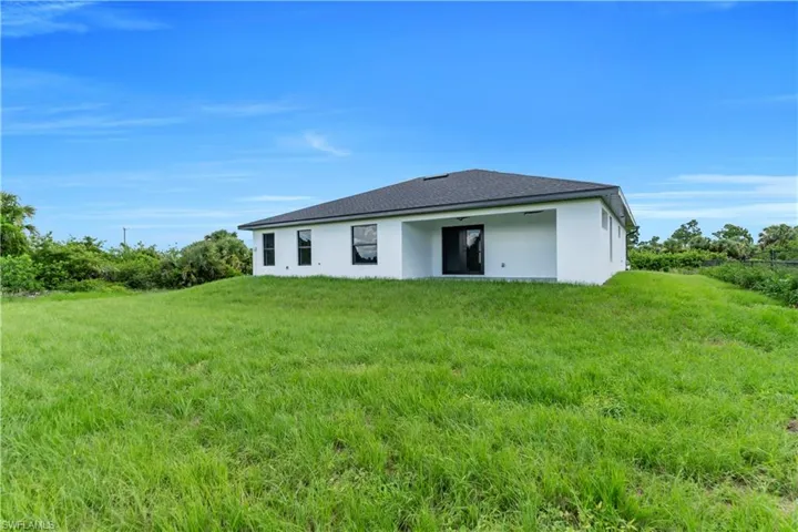 Back of house featuring stucco siding, a lawn, and a shingled roof