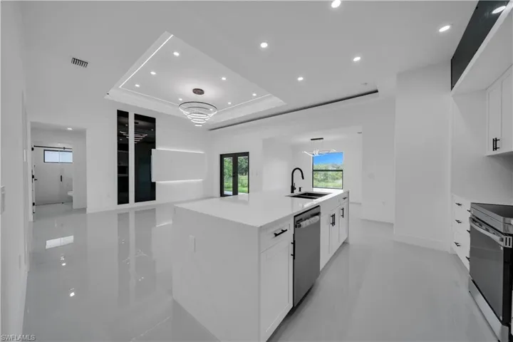 Kitchen featuring appliances with stainless steel finishes, white cabinetry, recessed lighting, a center island with sink, and a raised ceiling