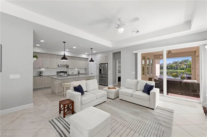 Open great room with TILE FLOOR, floor outlet, TRAY CEILING, and IMPACT GLASS sliding glass doors leading out to the lanai. NEW CEILING FAN (2017), NEW WINDOW BLINDS (2017), NEW KITCHEN PENDANTS (2023)