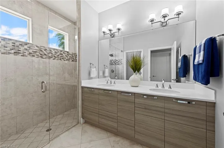 Luxurious primary bath with double sink CUSTOM ITALIAN CABINETRY vanity, solid surface counter, TILE FLOOR, large tile shower with tile to the ceiling, decorative listello tile detail, FRAMELESS GLASS SHOWER DOOR, and water closet.