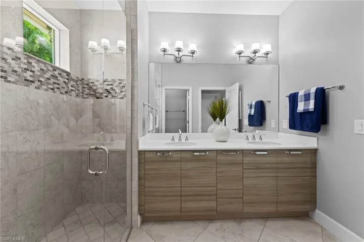 Luxurious primary bath with double sink CUSTOM ITALIAN CABINETRY vanity, solid surface counter, TILE FLOOR, large tile shower with tile to the ceiling, decorative listello tile detail, FRAMELESS GLASS SHOWER DOOR, and water closet.