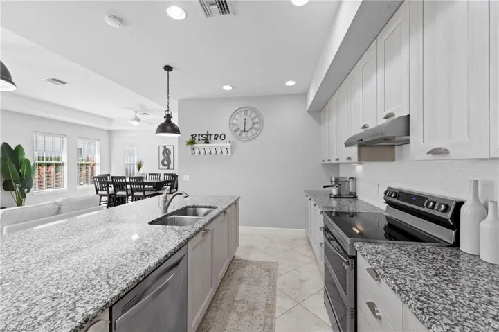 Open kitchen featuring CUSTOM ITALIAN CABINETRY, UNDER CABINET LIGHTING, TILE FLOOR, CONVECTION DOUBLE OVEN RANGE, MICROWAVE/OVEN combo, EXTERNALLY VENTED RANGE HOOD, center island with sink, light stone counters, and a breakfast bar. NEW BACKSPLASH (2019), NEW KITCHEN PENDANTS (2023), NEW APPLIANCES (2023)