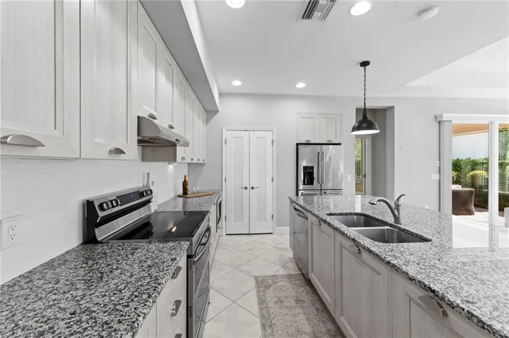 Open kitchen featuring CUSTOM ITALIAN CABINETRY, UNDER CABINET LIGHTING, TILE FLOOR, CONVECTION DOUBLE OVEN RANGE, MICROWAVE/OVEN combo, EXTERNALLY VENTED RANGE HOOD, center island with sink, light stone counters, and a breakfast bar. NEW BACKSPLASH (2019), NEW KITCHEN PENDANTS (2023), NEW APPLIANCES (2023)