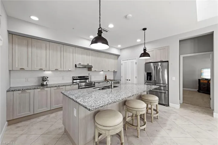 Open kitchen featuring CUSTOM ITALIAN CABINETRY, UNDER CABINET LIGHTING, TILE FLOOR, CONVECTION DOUBLE OVEN RANGE, MICROWAVE/OVEN combo, EXTERNALLY VENTED RANGE HOOD, center island with sink, light stone counters, and a breakfast bar. NEW BACKSPLASH (2019), NEW KITCHEN PENDANTS (2023), NEW APPLIANCES (2023)