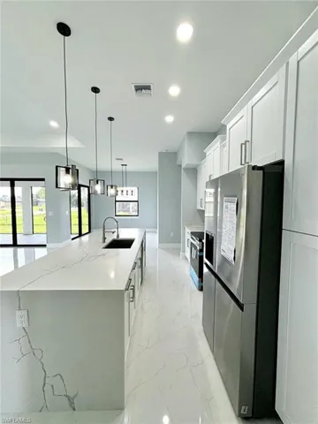 Kitchen with a large island with sink, appliances with stainless steel finishes, white cabinets, light stone countertops, and sink