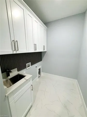 Clothes washing area featuring electric dryer hookup, sink, hookup for a washing machine, and cabinets
