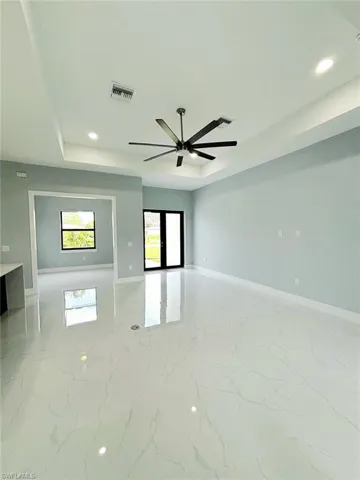 Empty room with a tray ceiling, light tile patterned floors, and ceiling fan