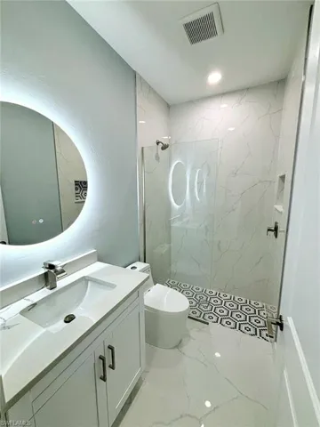 Bathroom with a tile shower, vanity, tile patterned flooring, and toilet