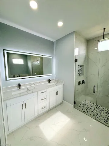 Bathroom featuring double vanity, a shower with door, tile patterned flooring, and a healthy amount of sunlight