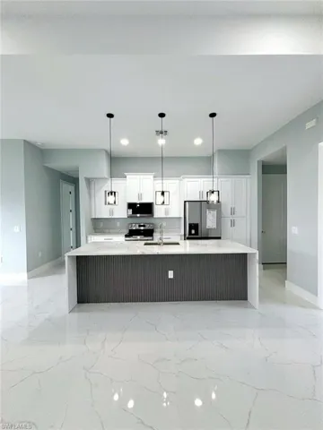 Kitchen with light tile patterned floors, appliances with stainless steel finishes, white cabinetry, a large island, and decorative light fixtures