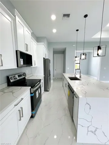 Kitchen with appliances with stainless steel finishes, light tile patterned floors, sink, and light stone countertops